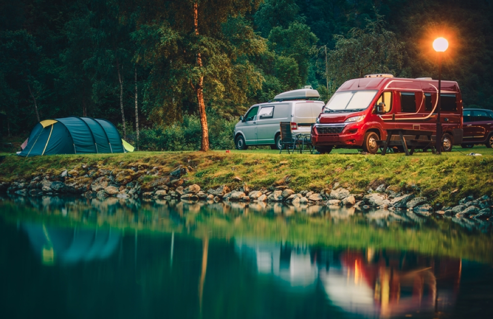 Camping vans and tents set up next to a lake