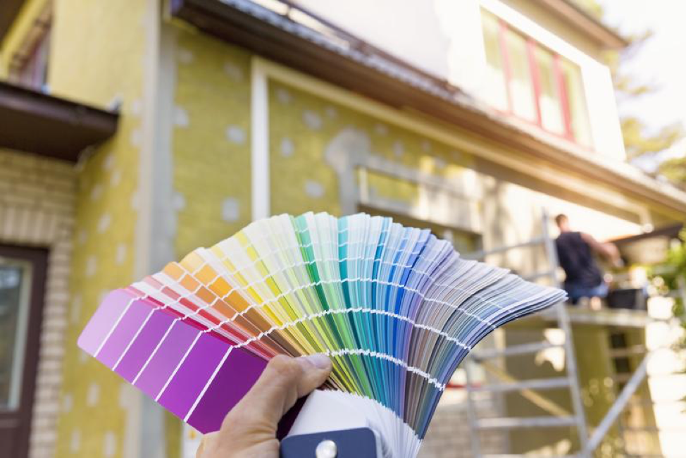 Many colors of paint samples held in a hand with a house in the background